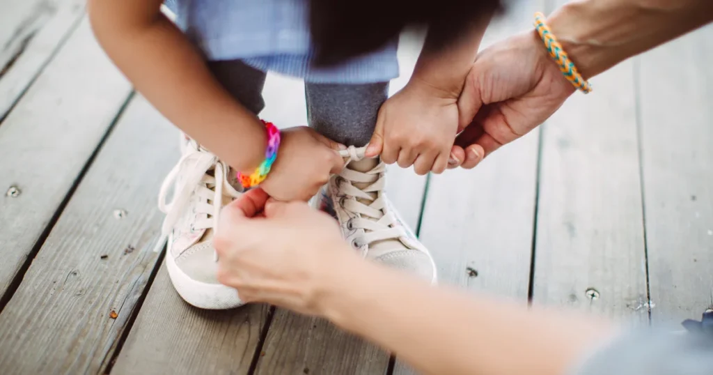A parent gently tying a child's sneakers, an example of acts of service for kids.