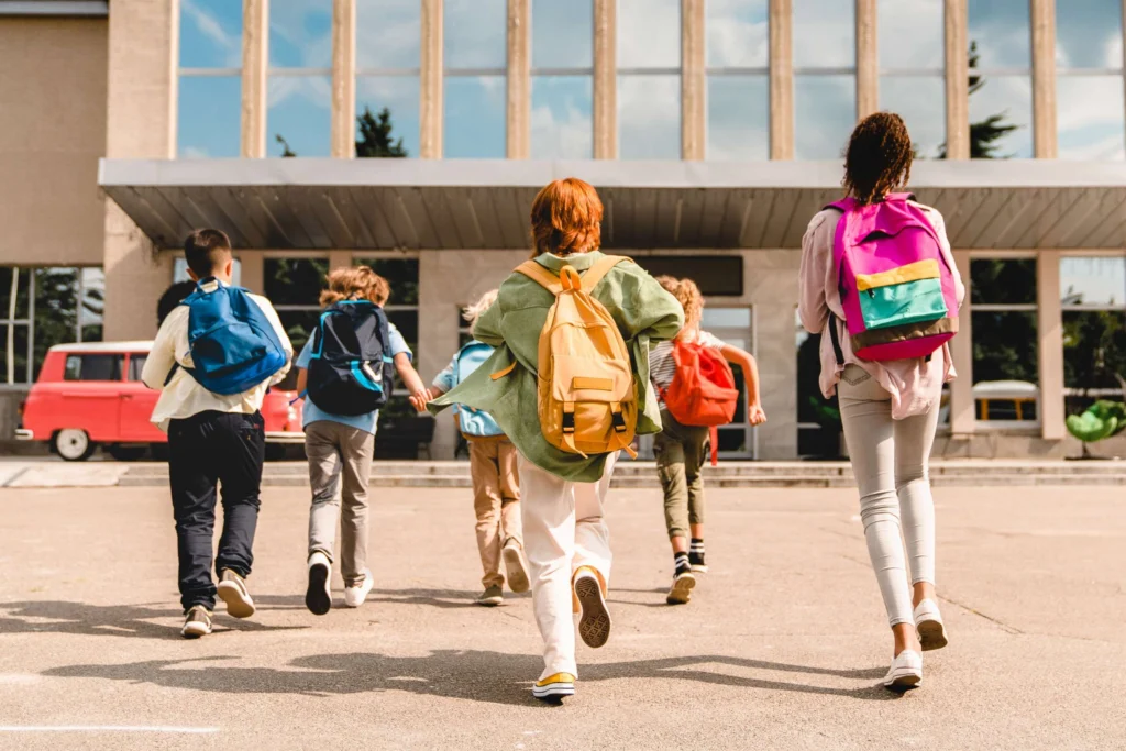 A child wearing a backpack looks toward a school, showing how physical development and gross motor skills prepare kids for the future.