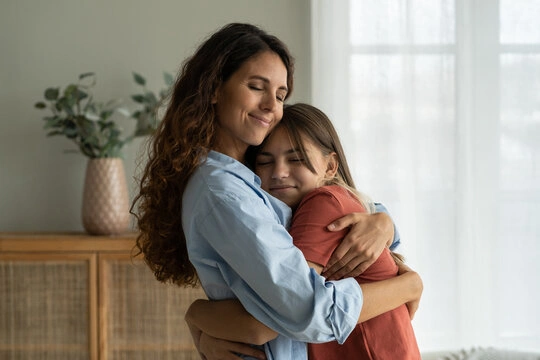A happy young girl hugging her mother tightly, showing signs of a secure parent-child bond.