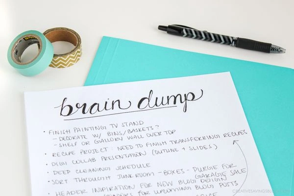 A parent writes a quick 'brain dump' list on a notepad to clear their mind as an act of self-care.