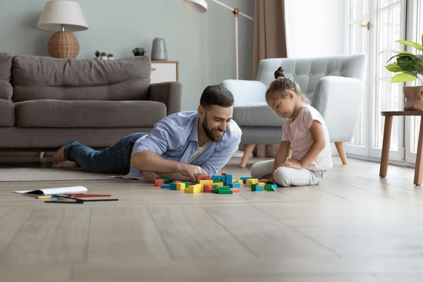 A father sitting on the floor giving his daughter undivided attention while playing with blocks.