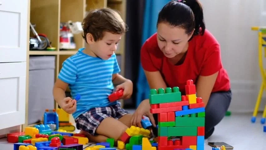 A mother playing blocks with her son on the floor, demonstrating quality time without distractions.