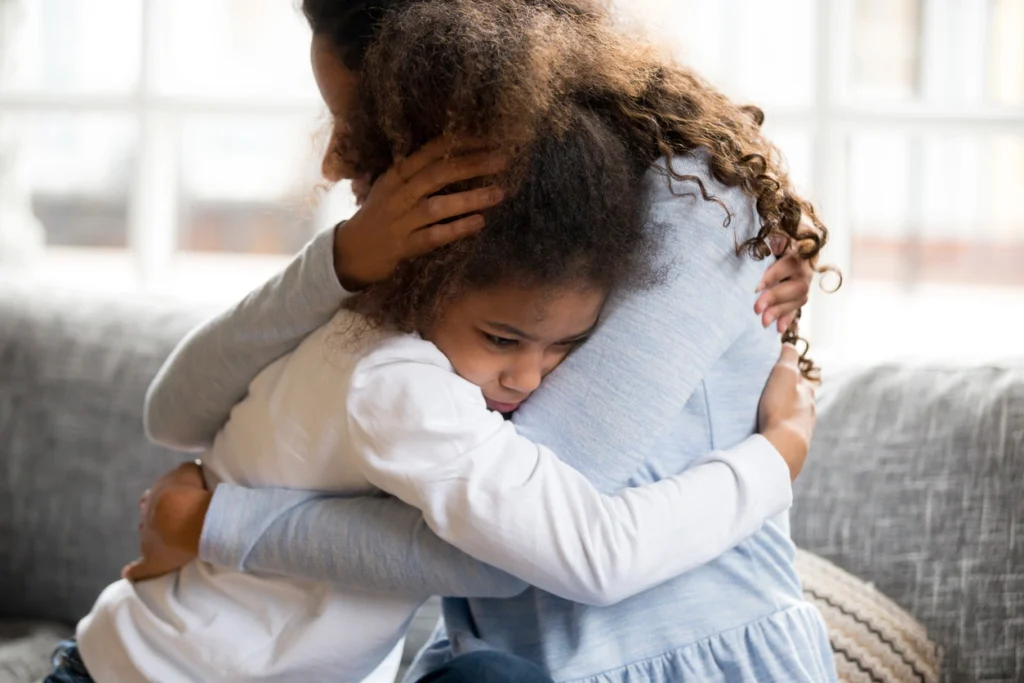 A parent kneels down to comfort their child, modeling how to repair a relationship after a conflict.