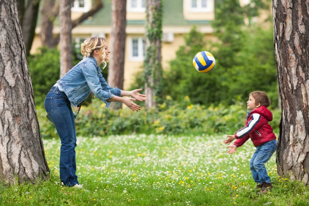 A parent plays with their toddler by rolling a ball in the yard, a fun way to encourage gross motor skills.