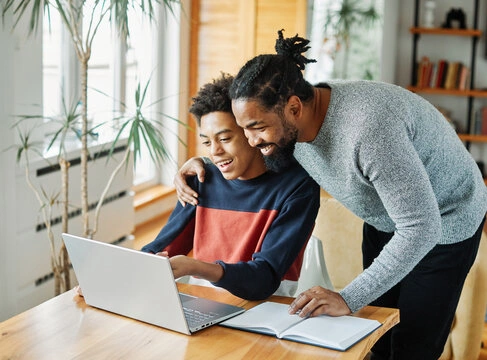 A parent listening to a teenager explain a plan on a laptop, demonstrating the consultant parenting style.
