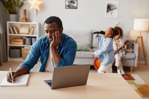 A parent juggles a laptop, phone, and toy, representing the mental load that contributes to high-functioning anxiety.