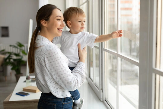 A parent stands thoughtfully looking out a window, reflecting after a long day.