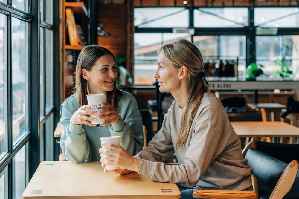 Two friends' hands on a table with coffee mugs, symbolizing seeking and receiving support for parental anxiety