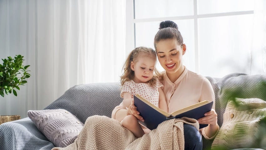  A mother reading a book for self-care while her children play independently nearby.