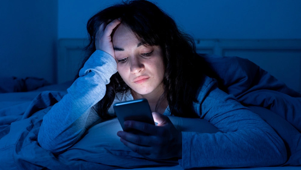 A worried parent scrolling through their phone at night, experiencing social comparison anxiety.