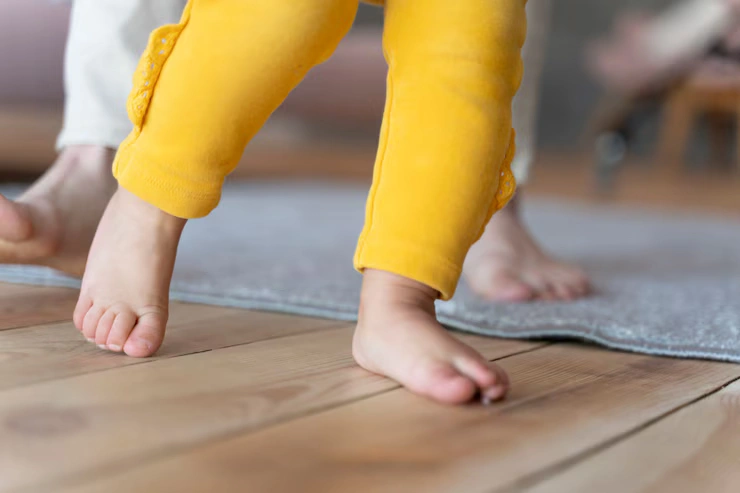 The feet of a toddler taking their first steps on a rug, an important early gross motor skill.