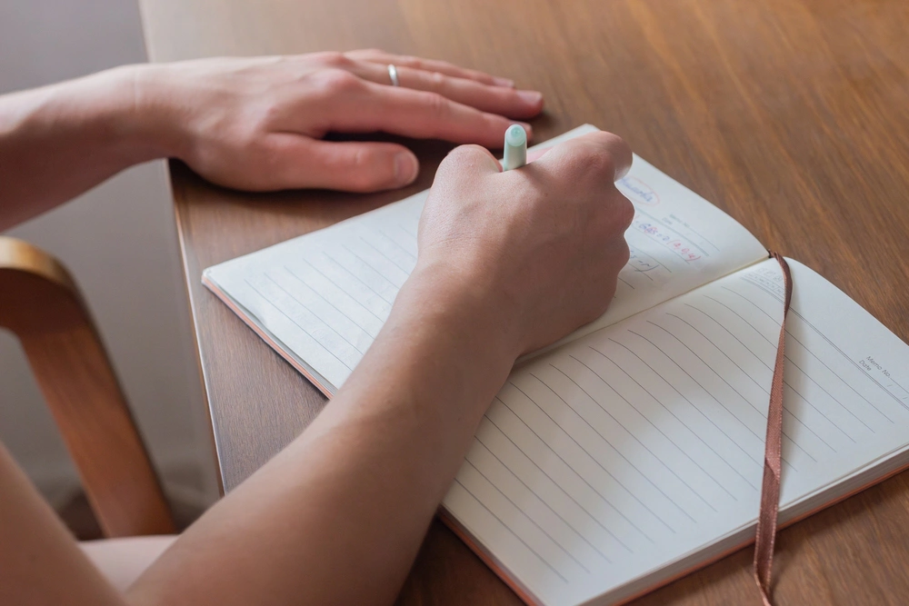 A close up of a person writing quickly in a journal to relieve stress.