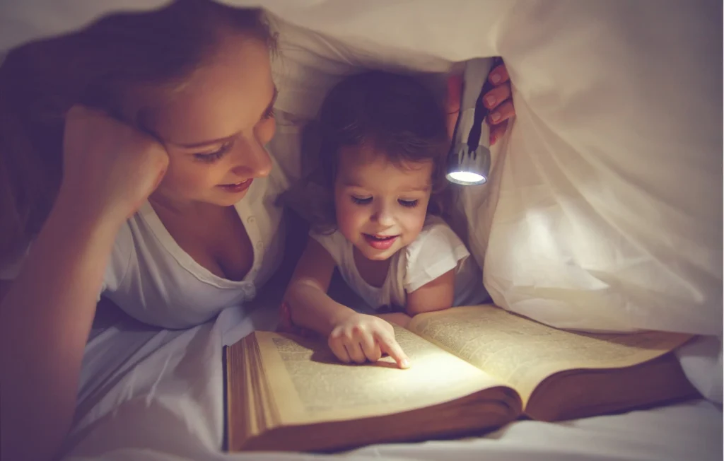 A parent reading a bedtime story to a child in a dimly lit room.