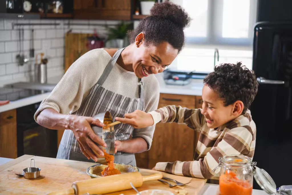 A parent and young child laughing while preparing dinner together in the kitchen.