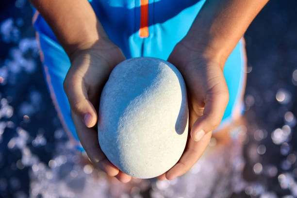 A close-up of hands holding a smooth, gray grounding stone, a tool used for sensory input in an anxiety toolkit.