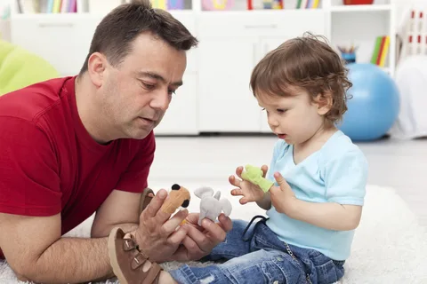 A toddler handing a toy to their father, illustrating the serve and return concept of language building.