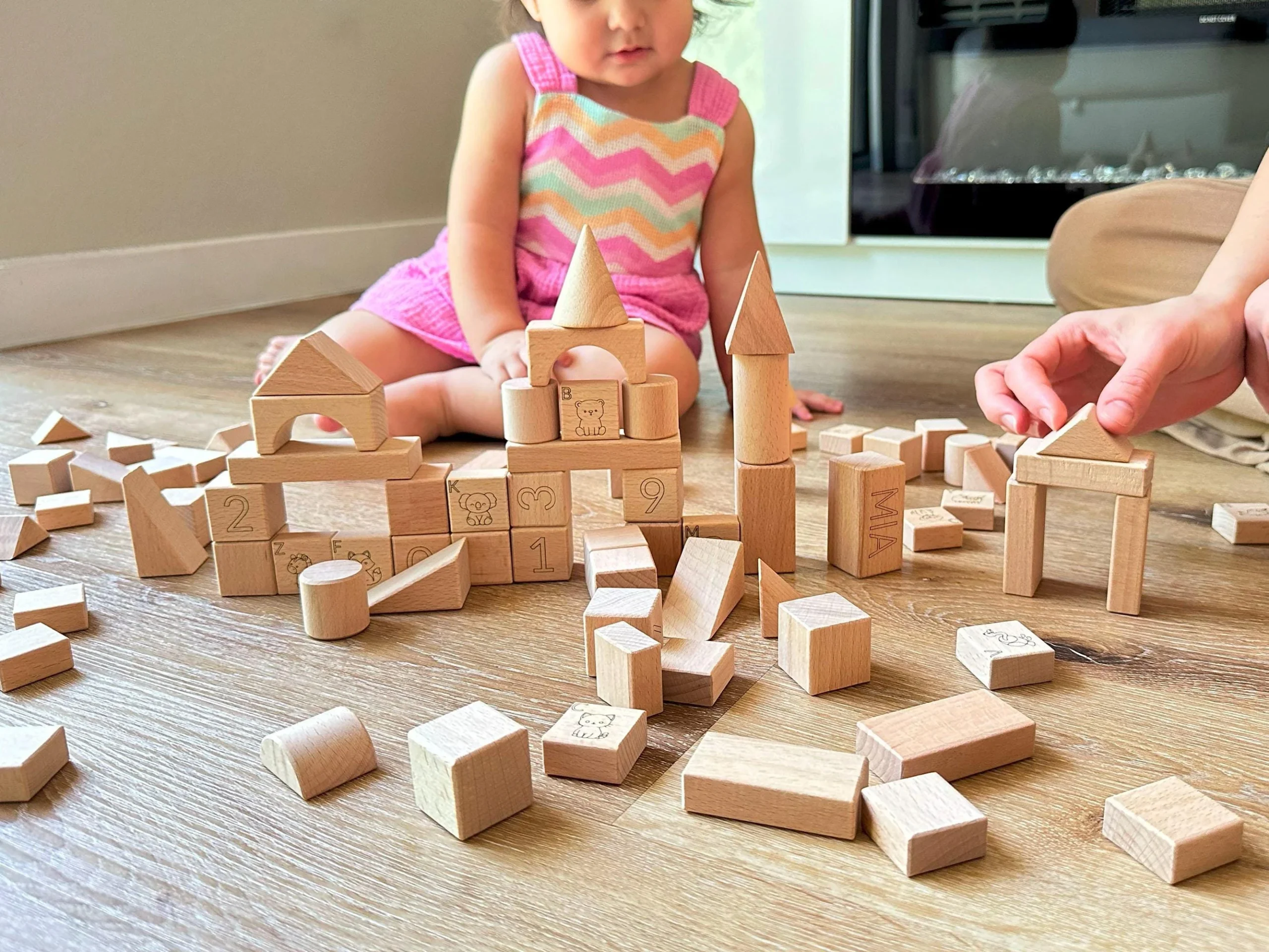 A young child building with wooden blocks on a sunlit floor during screen-free analog play