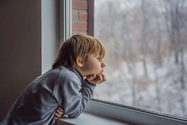 A young child sitting alone looking out a window, illustrating the quiet emotional impact of adverse childhood experiences