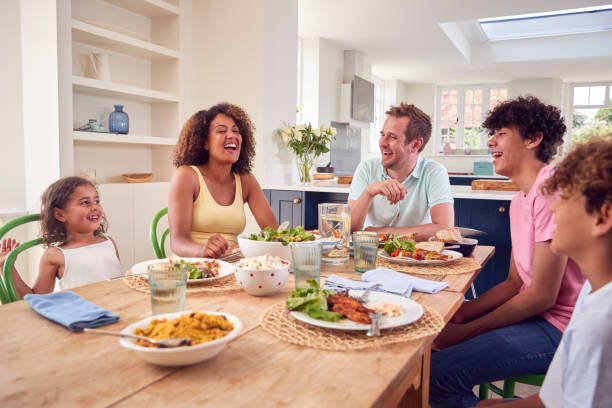 A family sitting at table smiling happily and have food infront of them, enjoying bonding over dining table