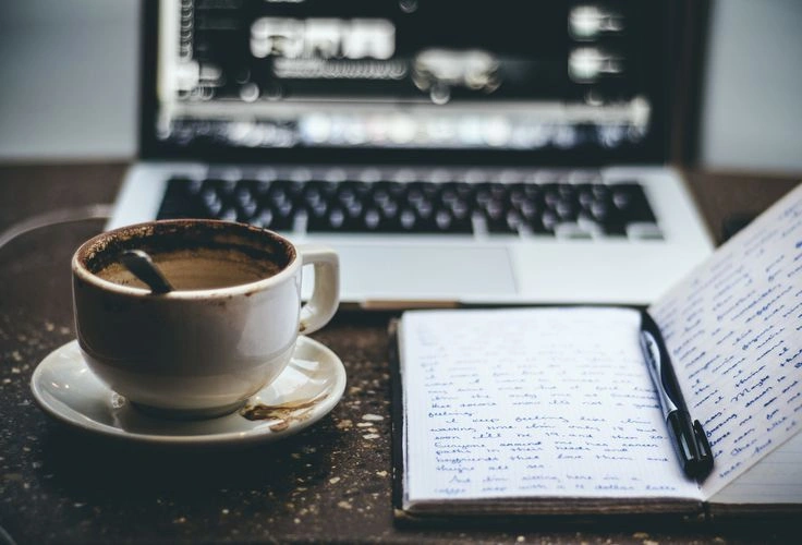 A journal, cup of tea, and wellness app on a phone arranged on a table, representing self-help tools parents use to manage anxiety.