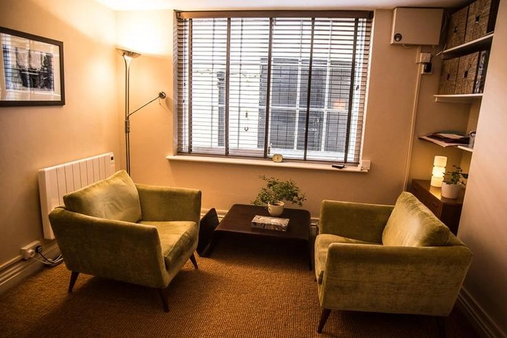 A warm and welcoming therapy office with two comfortable chairs, soft lighting, and a bookshelf, showing what a therapy space looks like.
